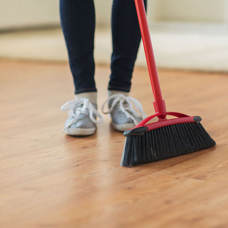Woman with broom sweeping floor at home | Leon Country Floors & More